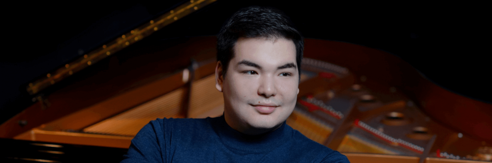 Alim Baisembayev leaning against the keys of a piano.